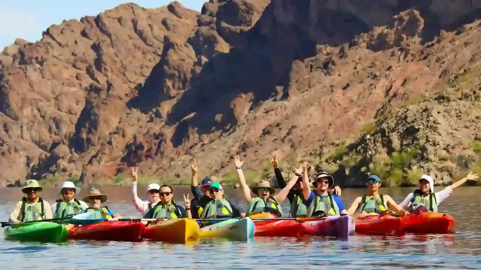 Large group of kayakers with canyon mountains behind them
